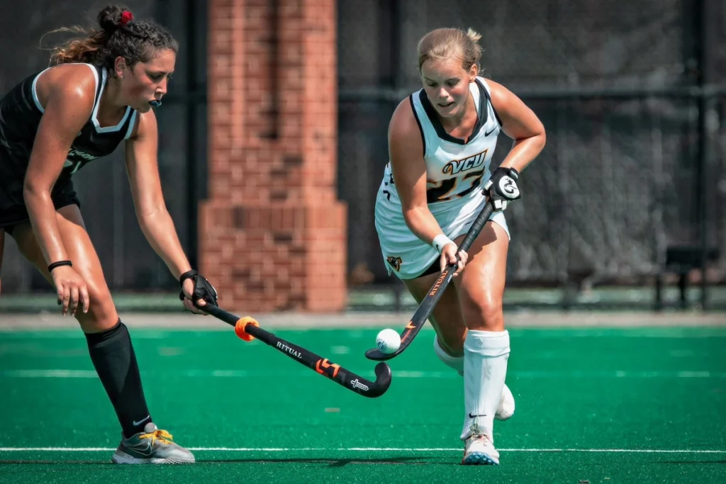 Dos jugadoras de hockey hierba compitiendo por la pelota durante un partido.